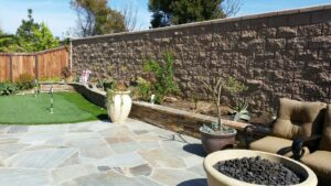 backyard with retaining wall, artificial grass, a fire bowl, and paver patio