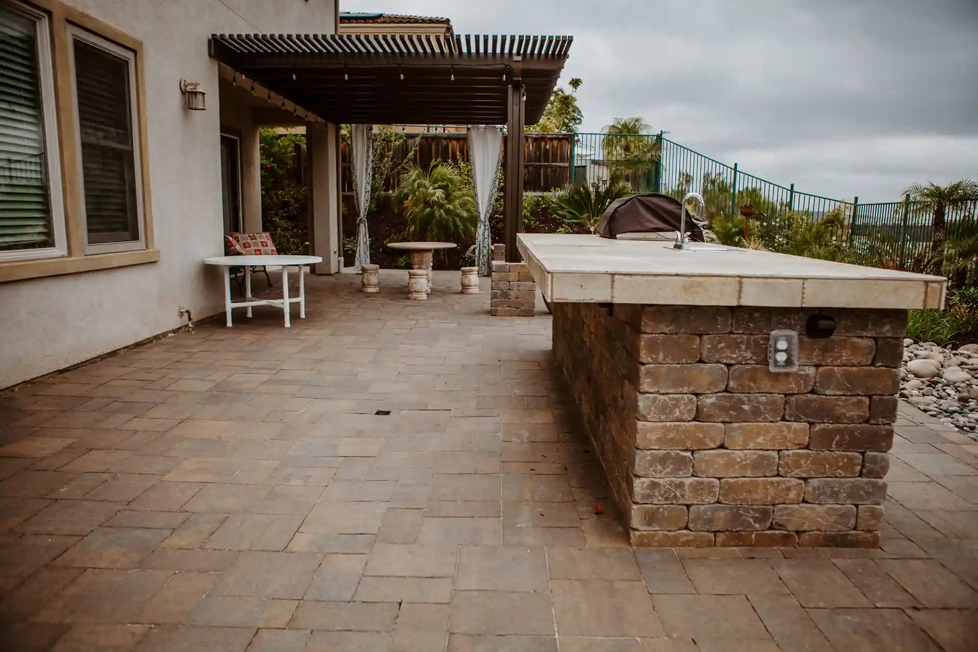 Photo of outdoor patio featuring stone island countertop and pergola covering. 