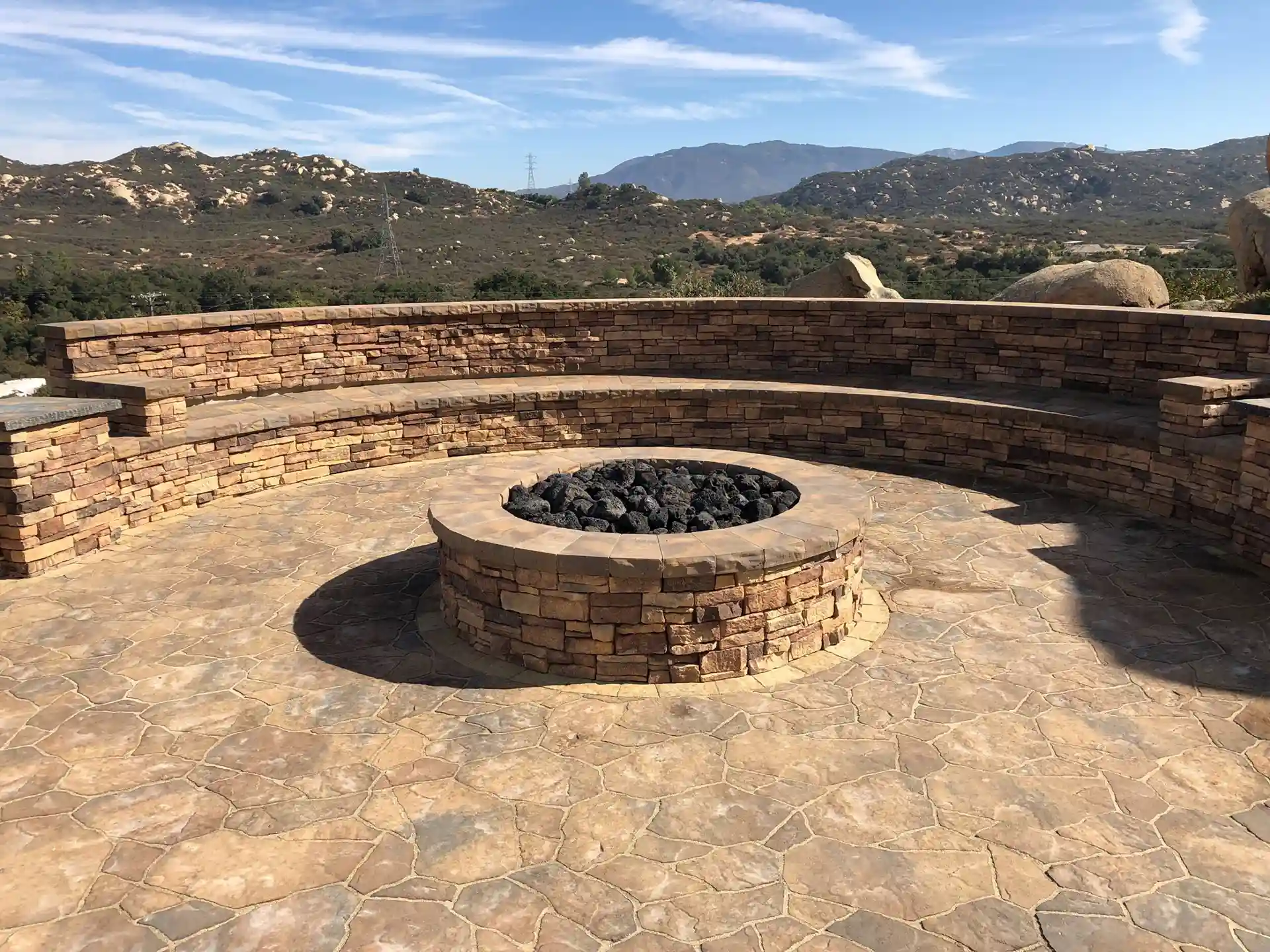 Photo of circular stone fire pit area with curved built-in seating wall. 