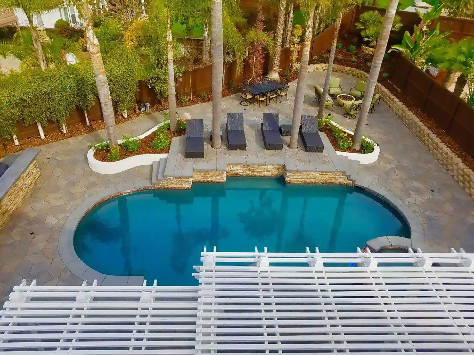 beautifully designed pool area with stone patio, palm trees, and a shaded seating area